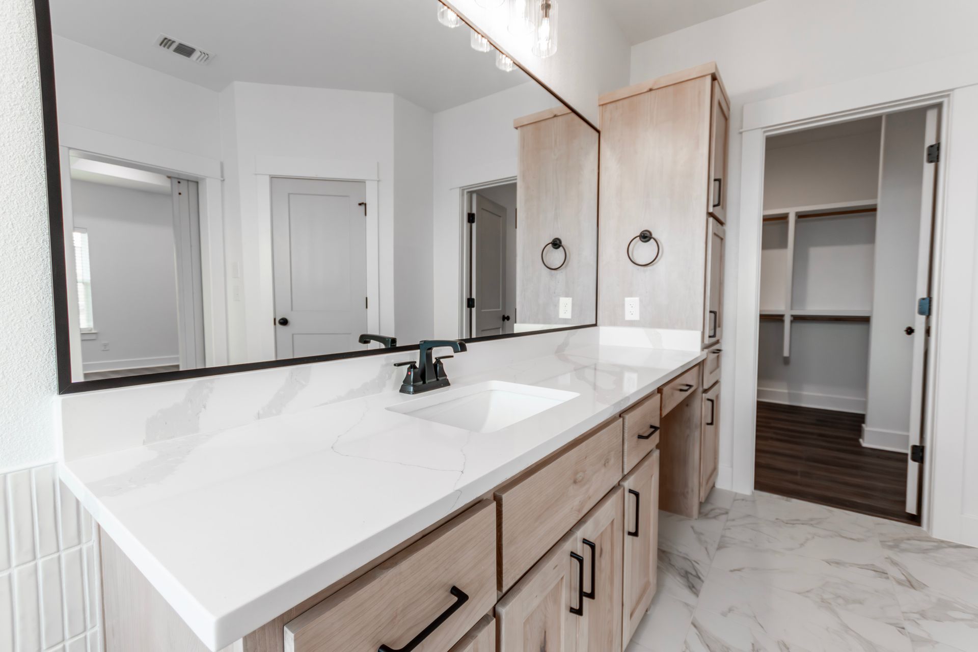 Bathroom with white countertop, light wood cabinets, large mirror, and open closet.