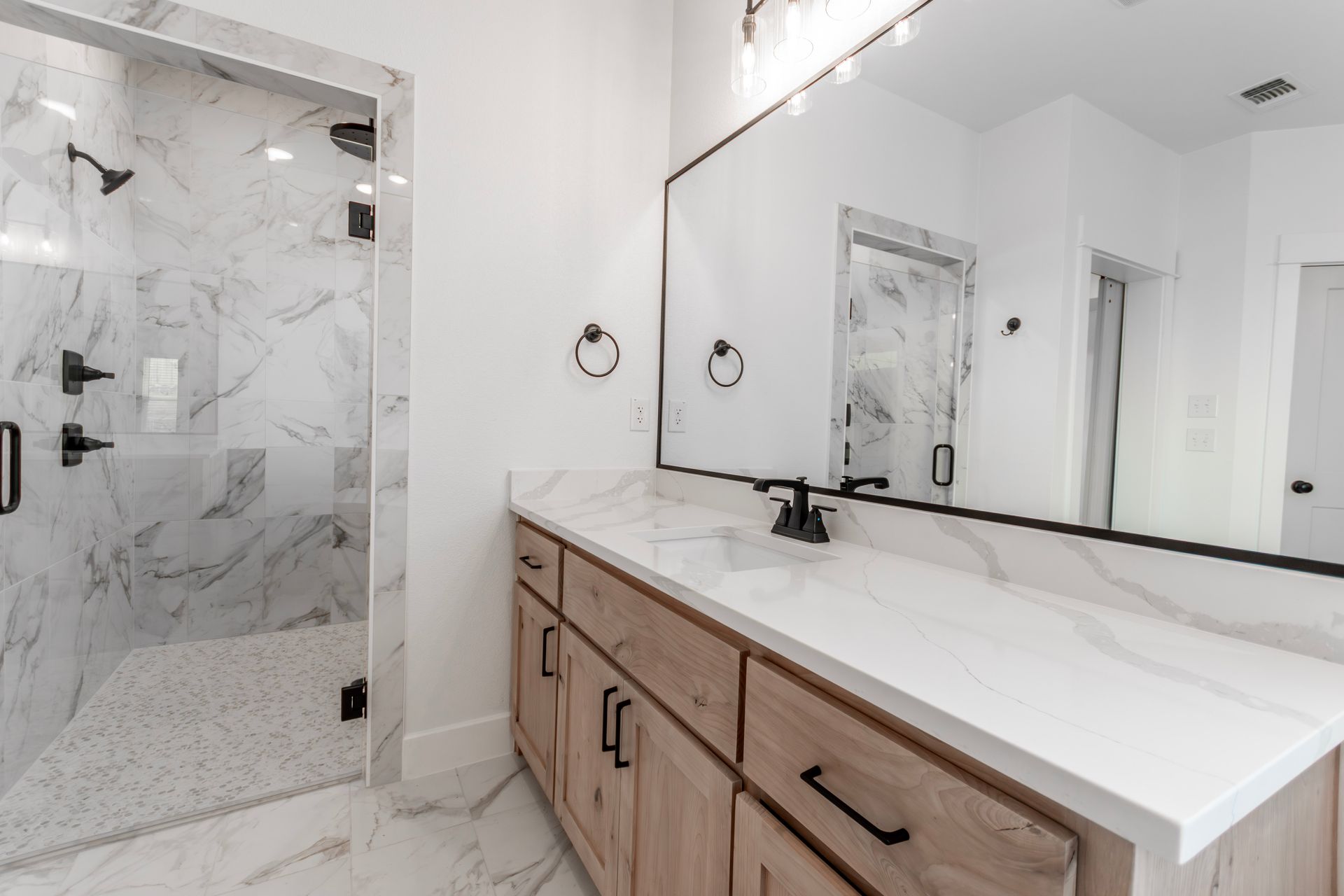Modern bathroom with marble shower, white countertop, and wood cabinets.