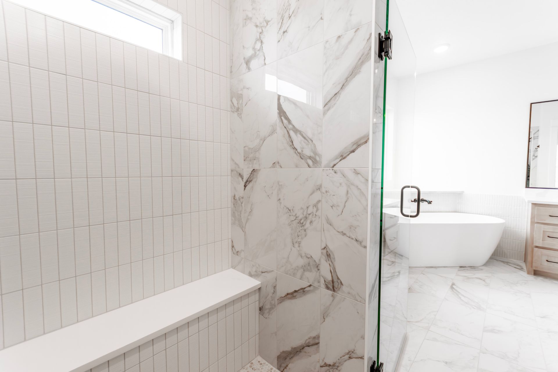 Modern bathroom with marble shower, white tiles, glass door, and freestanding tub.