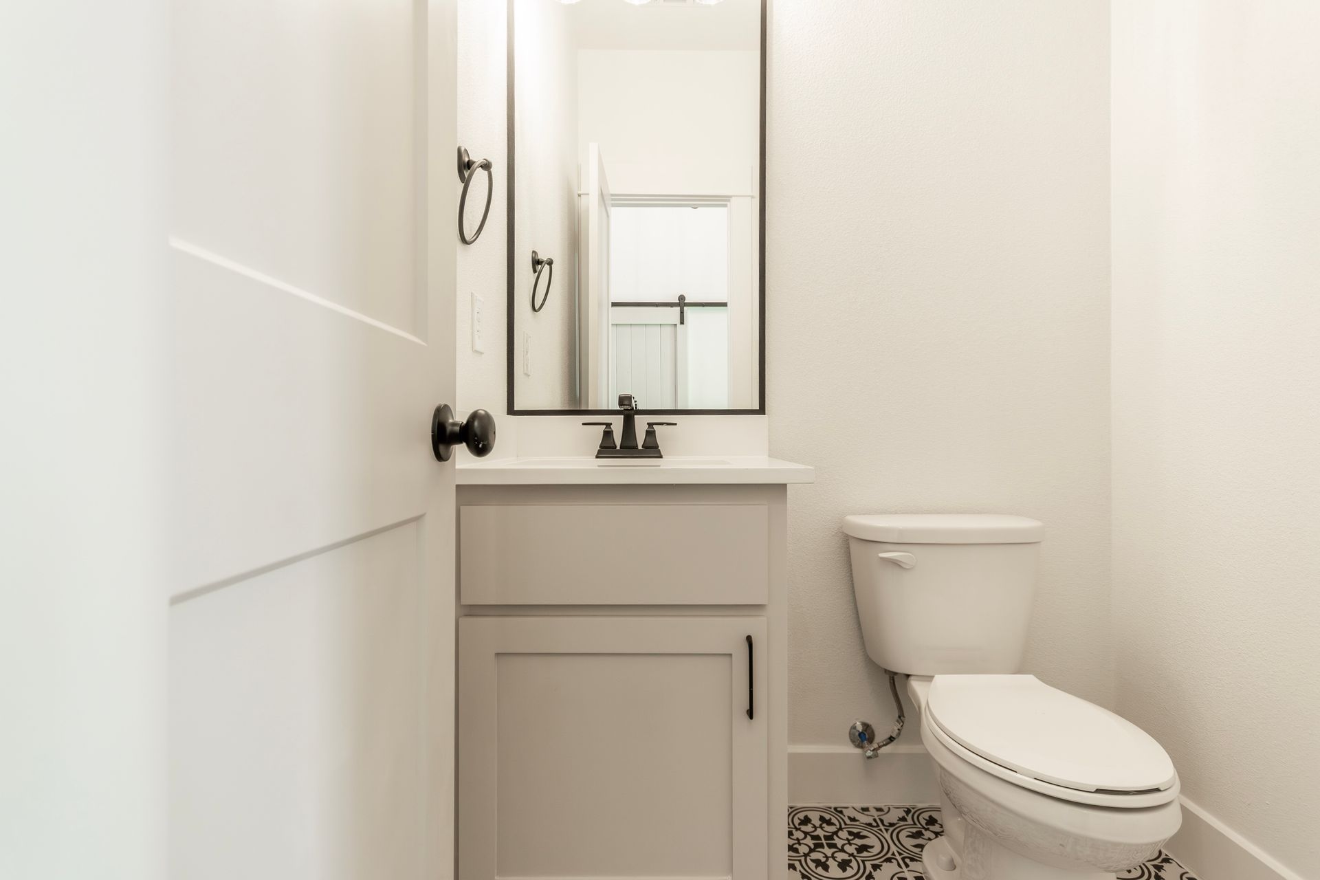 White bathroom with toilet, vanity, and black accents; patterned floor.