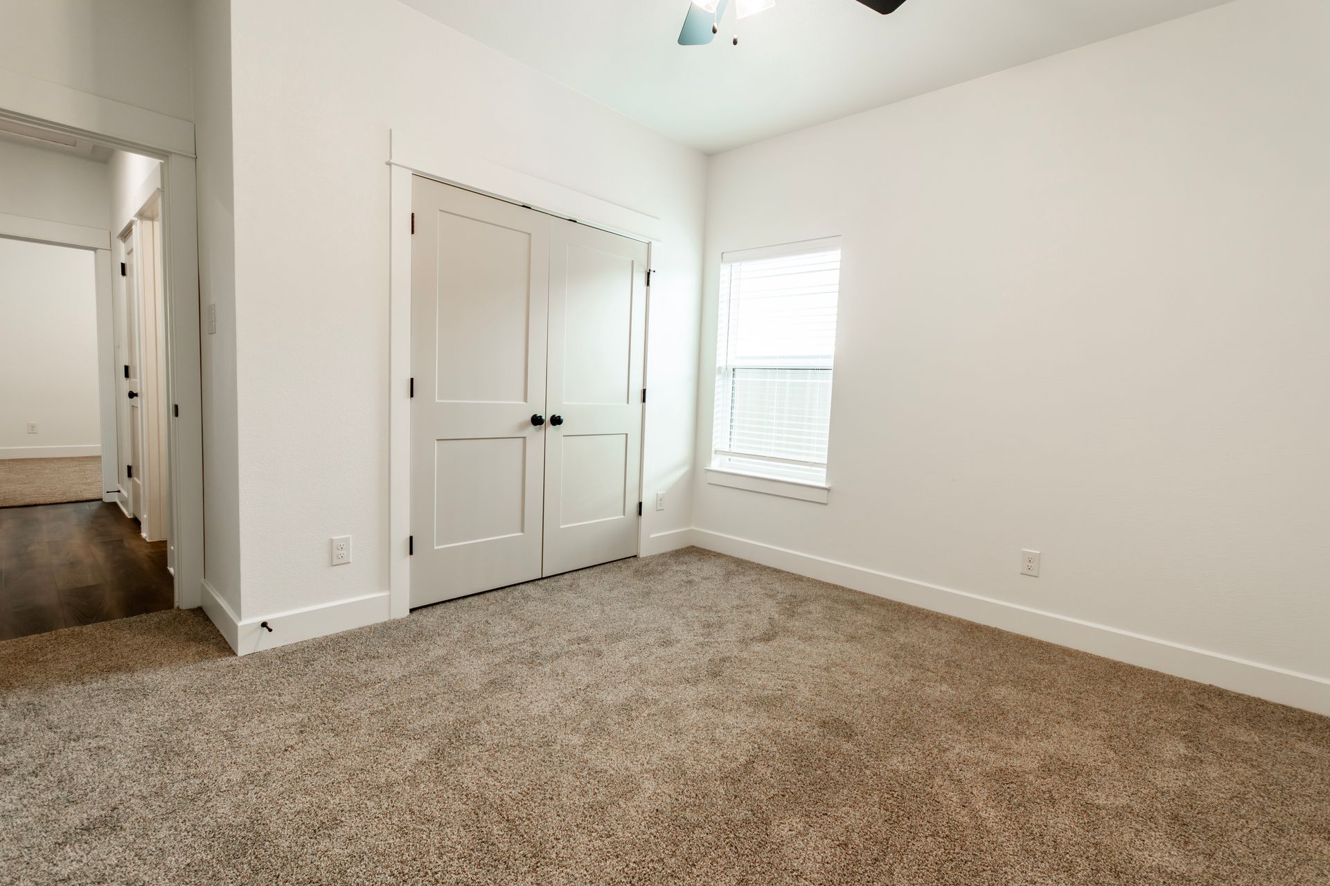 Empty room with white walls, closet doors, carpet, and a window.