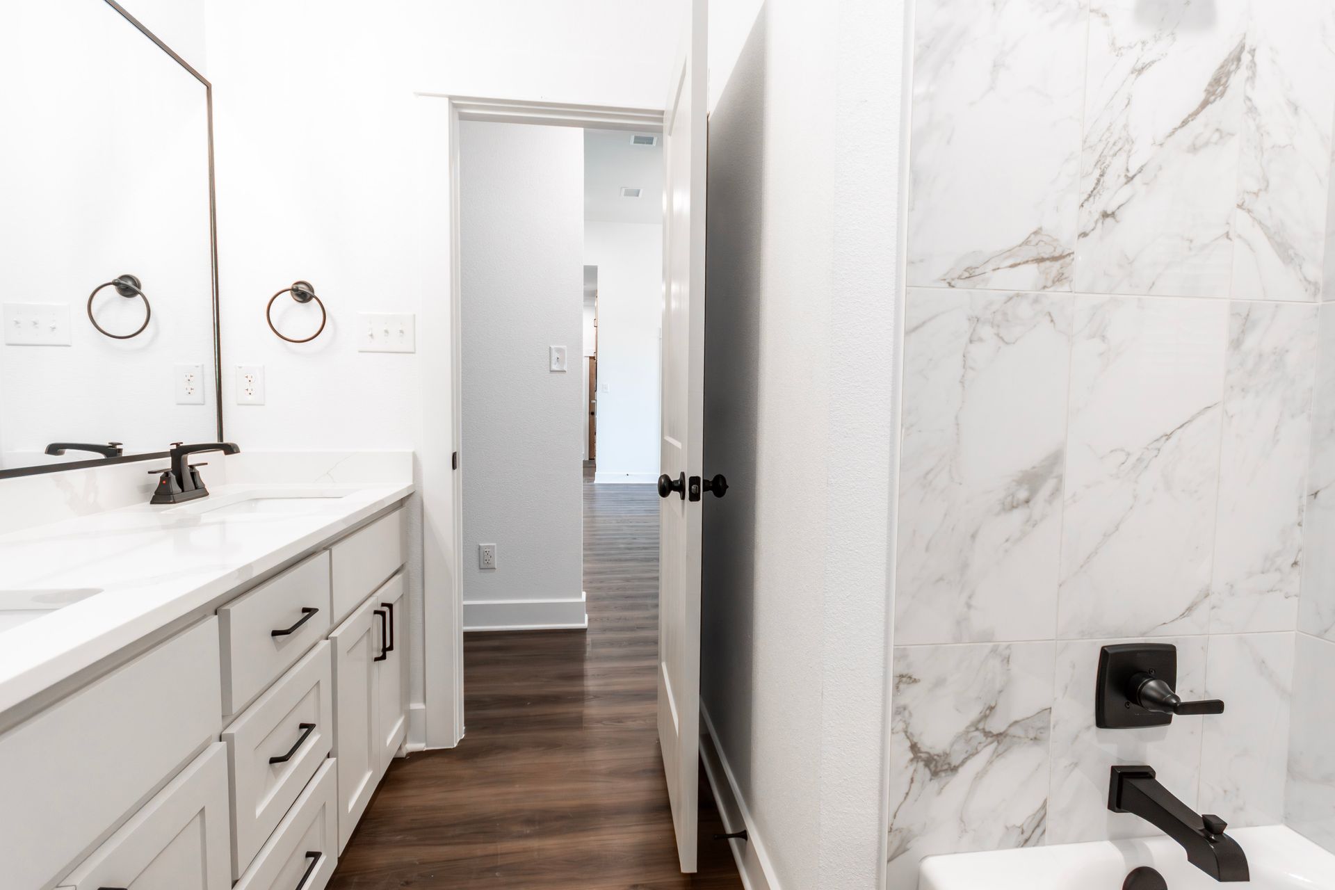 White bathroom with marble shower, vanity, and open door to hallway.