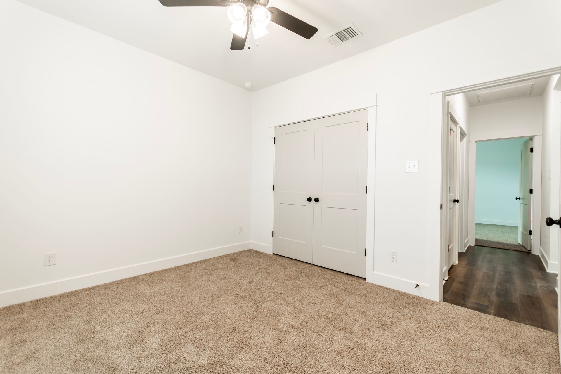 Empty bedroom with tan carpet, white walls, closet doors, and doorway to a hallway.