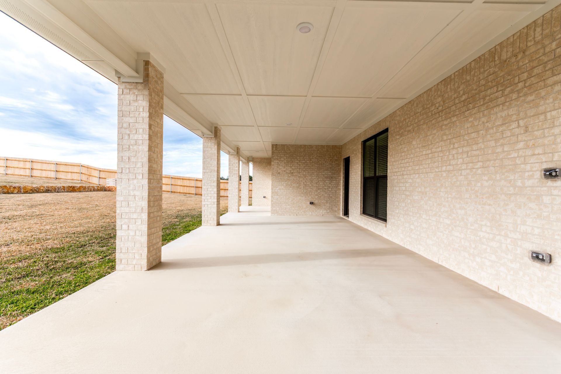 Covered patio with stone columns and walls, overlooking a field.