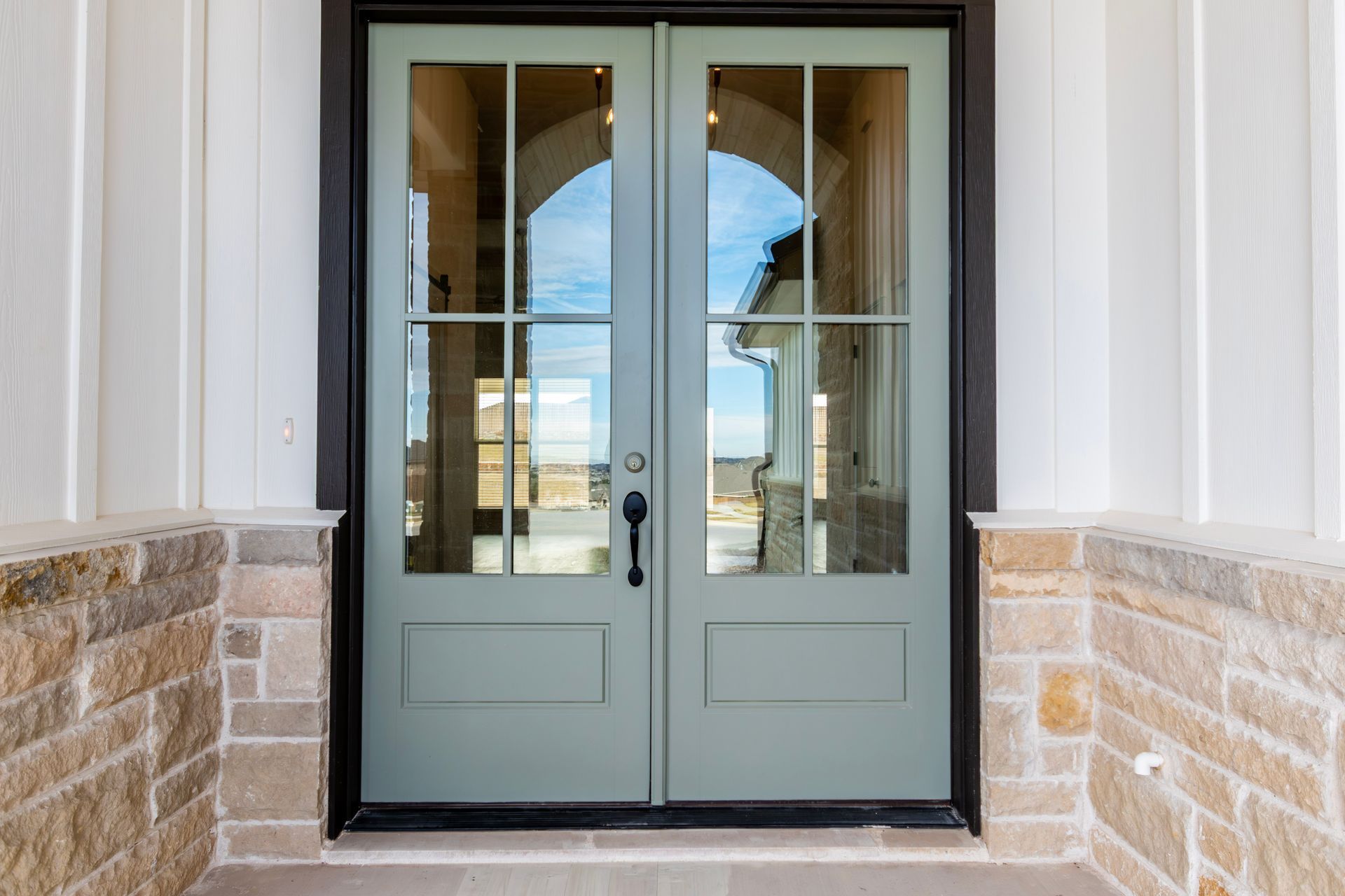 Green double doors with glass panels and black trim, set in a stone and white-paneled facade.