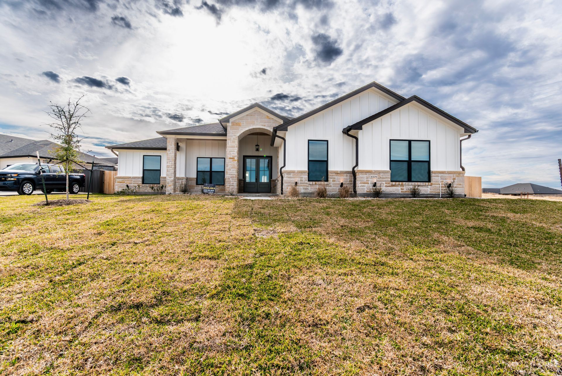 White farmhouse with black window frames, beige stone accents, and brown grass.