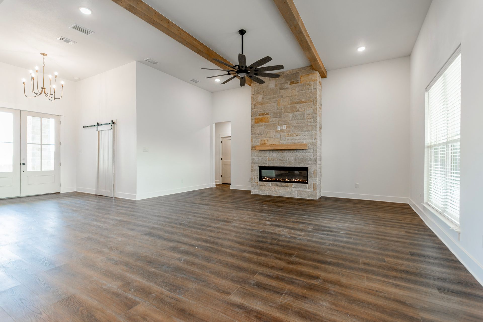 Spacious living room with stone fireplace, wooden beams, ceiling fan, and hardwood floors.