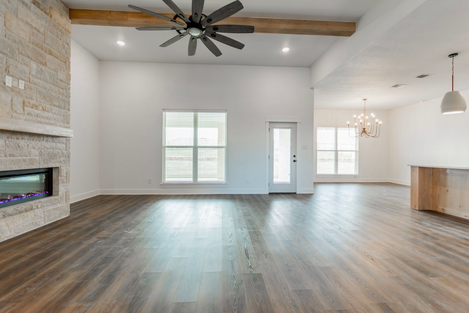 Spacious living room with stone fireplace, dark wood floors, white walls, and large windows.