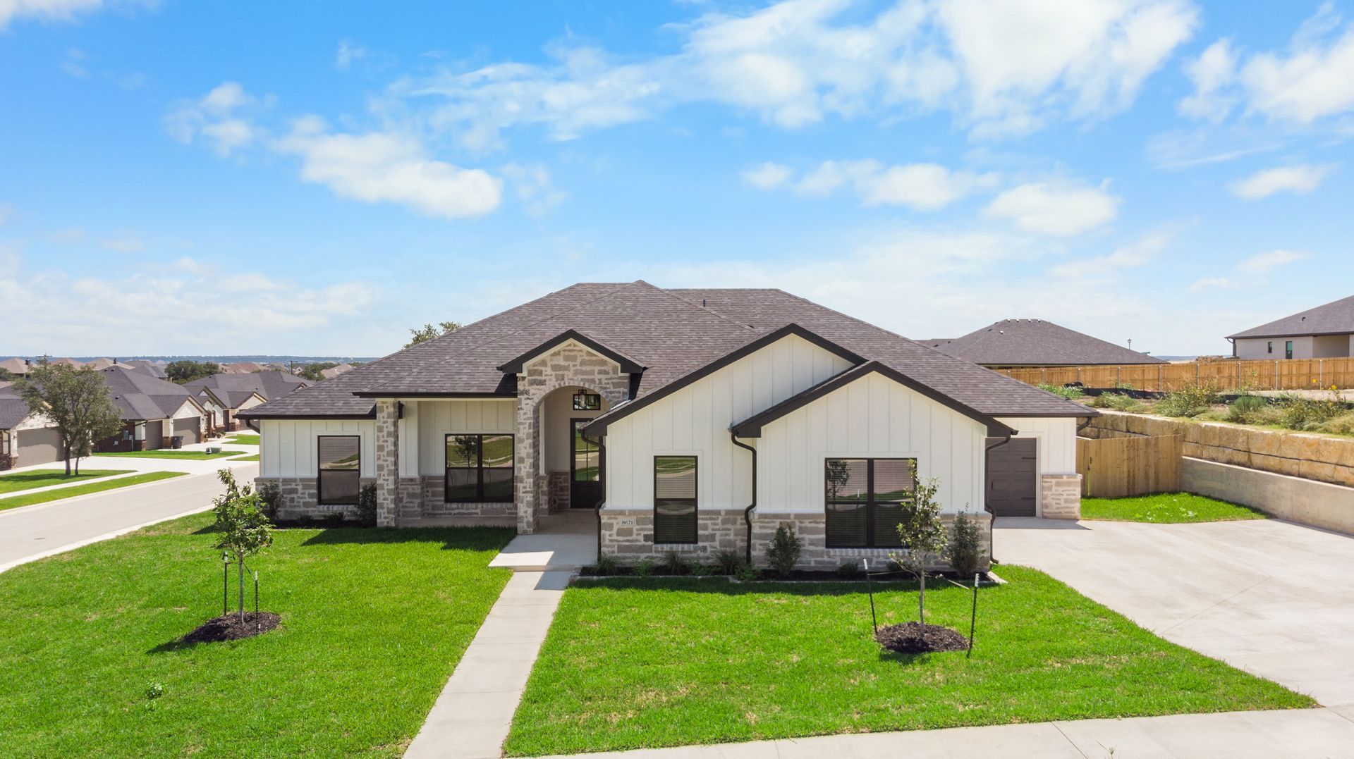 Modern white house with stone accents, green lawn, and blue sky.
