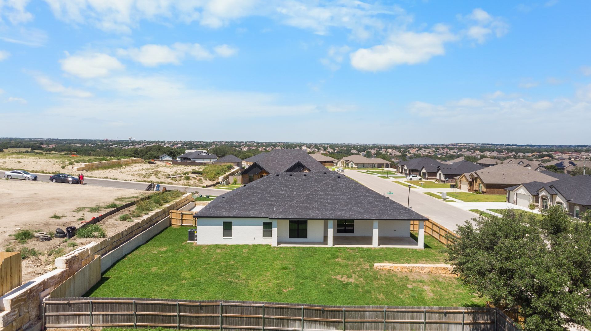 Aerial view of a modern white house with a dark roof, green yard, and a blue sky.