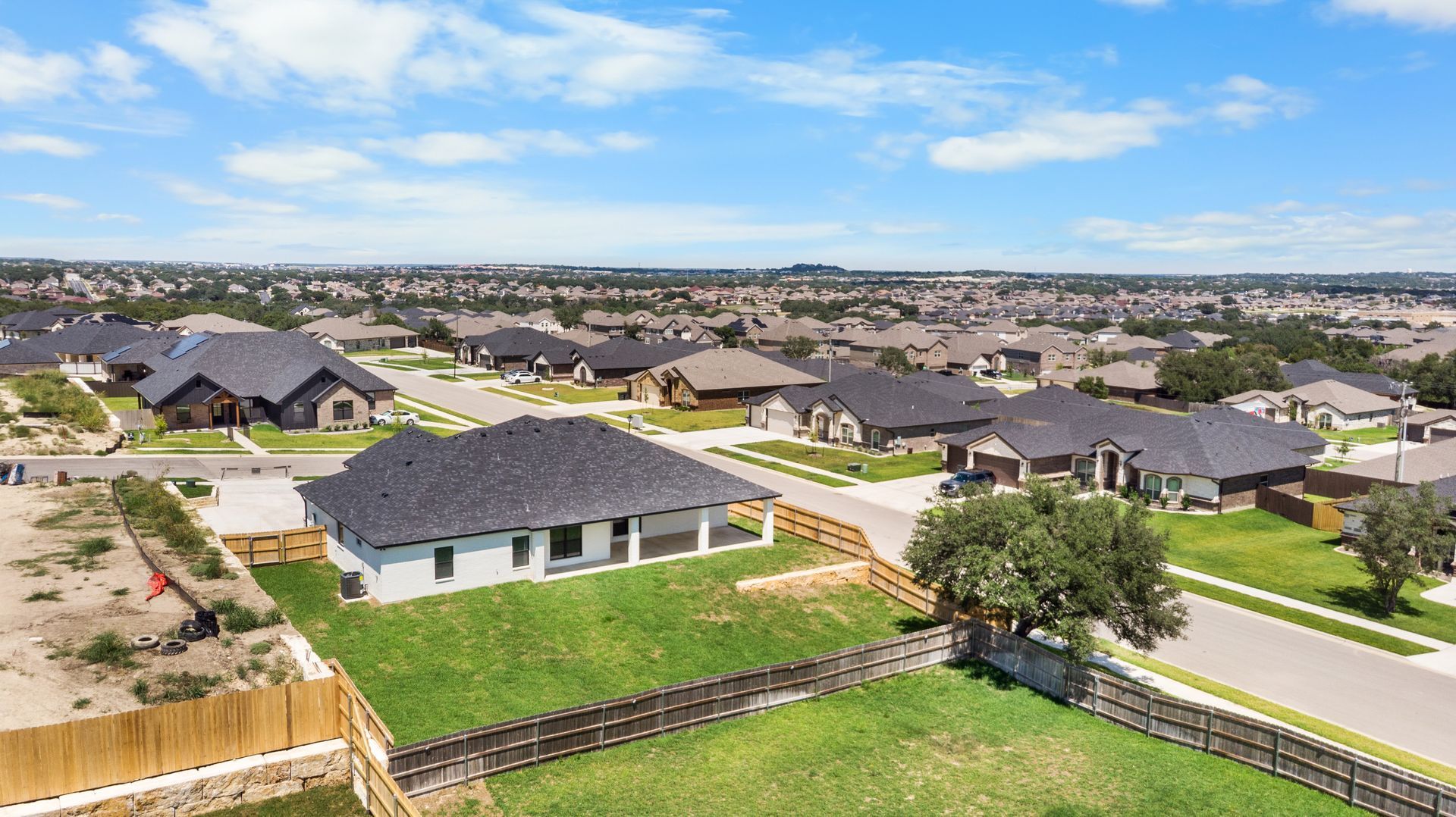 Aerial view of a suburban neighborhood with houses, roads, and green lawns under a blue sky.