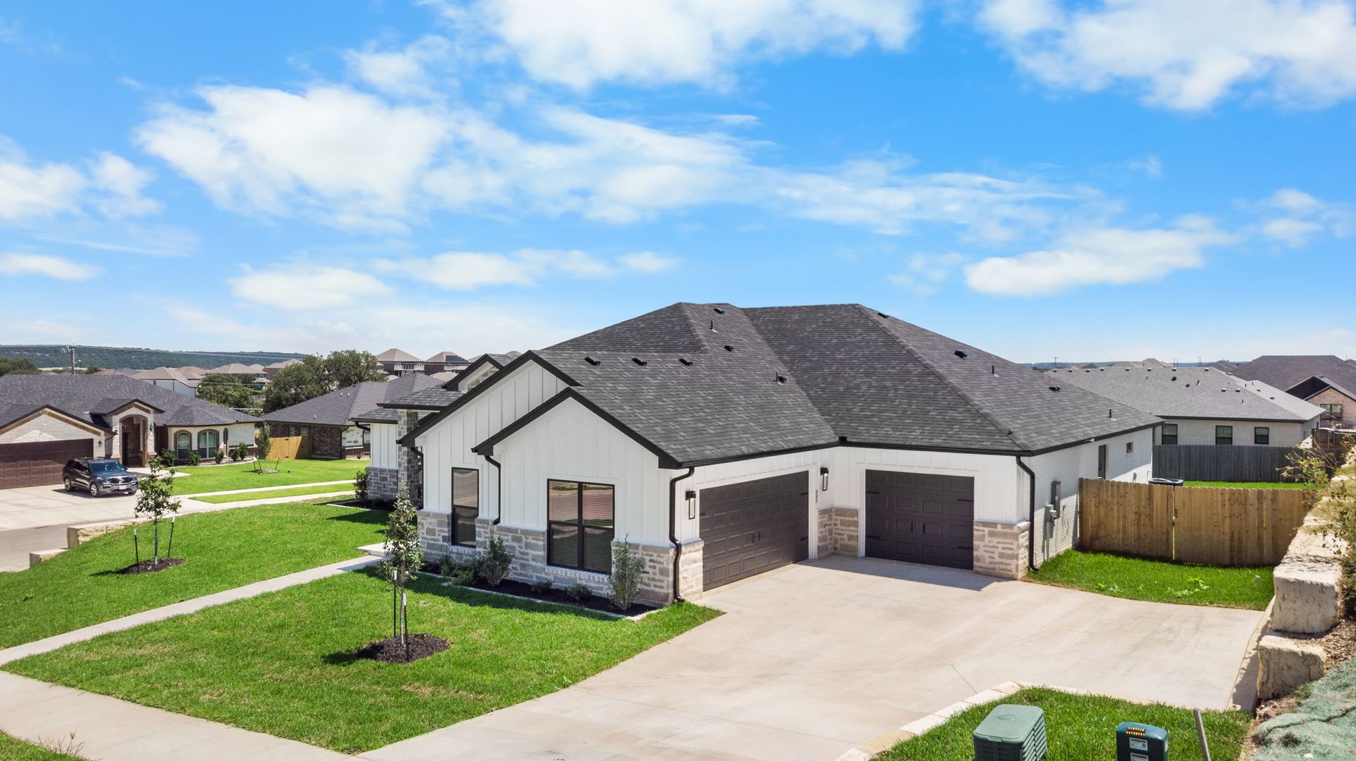 Modern white house with black roof, two-car garage, and green lawn under a blue sky.