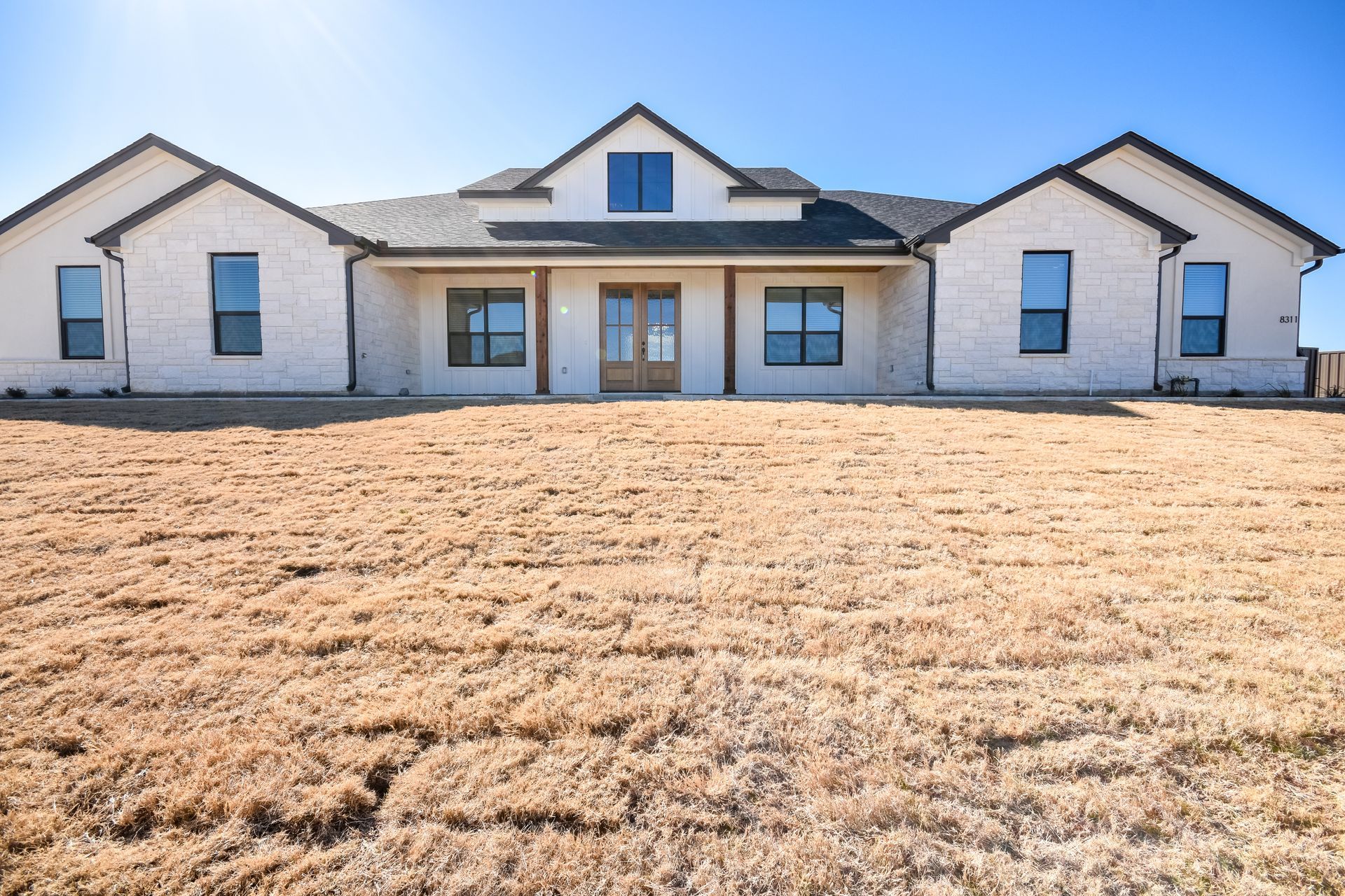 White house with gray roof and garage, light brown grass, clear blue sky.