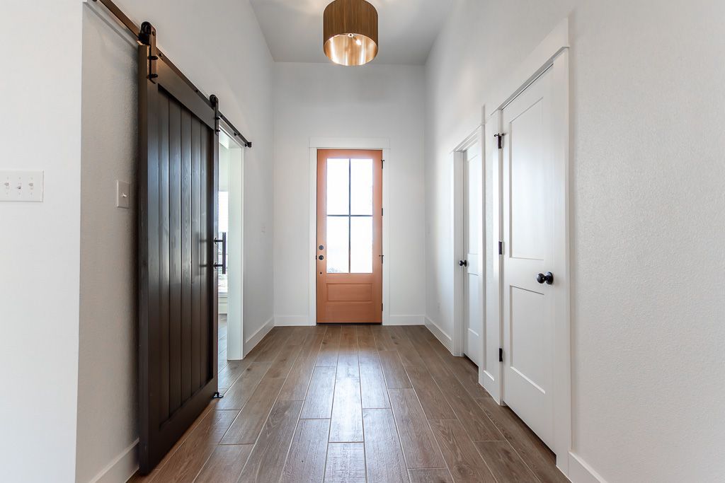 Hallway with wooden floor, white walls, brown barn door, and a light wooden door at the end.