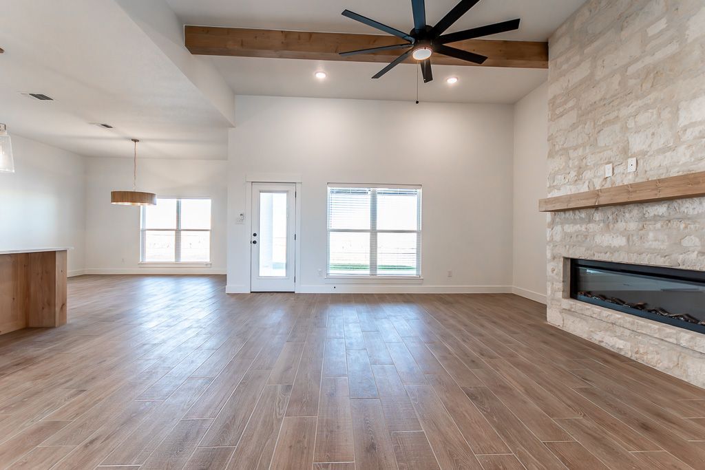 Spacious living room with stone fireplace, wooden beams, windows, and hardwood floors.