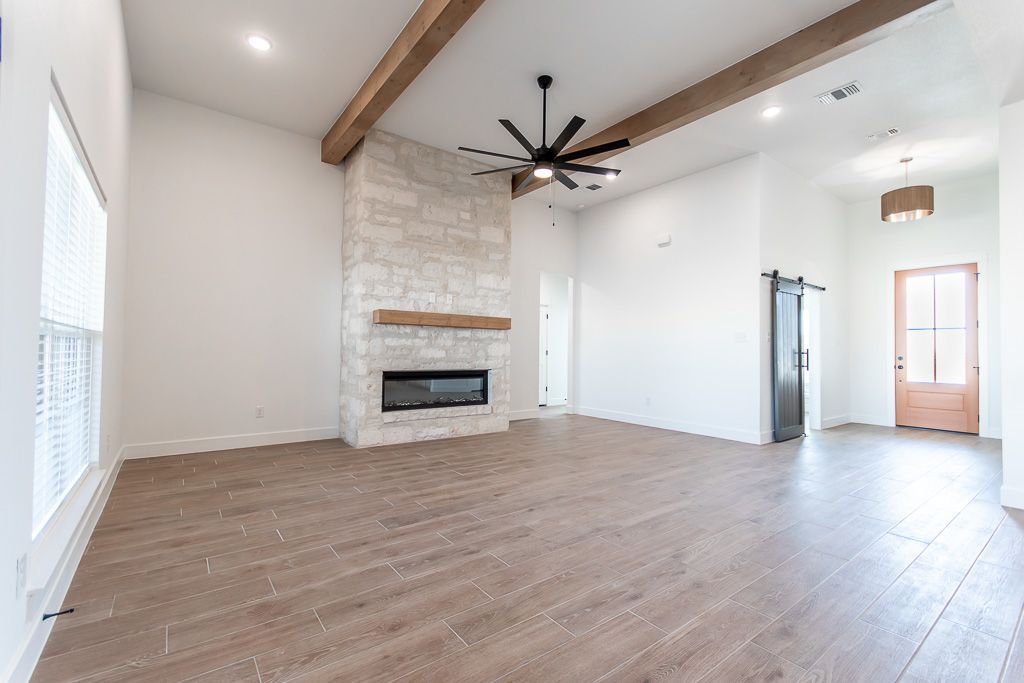 Spacious living room with stone fireplace, wooden beams, hardwood floors, and a ceiling fan.
