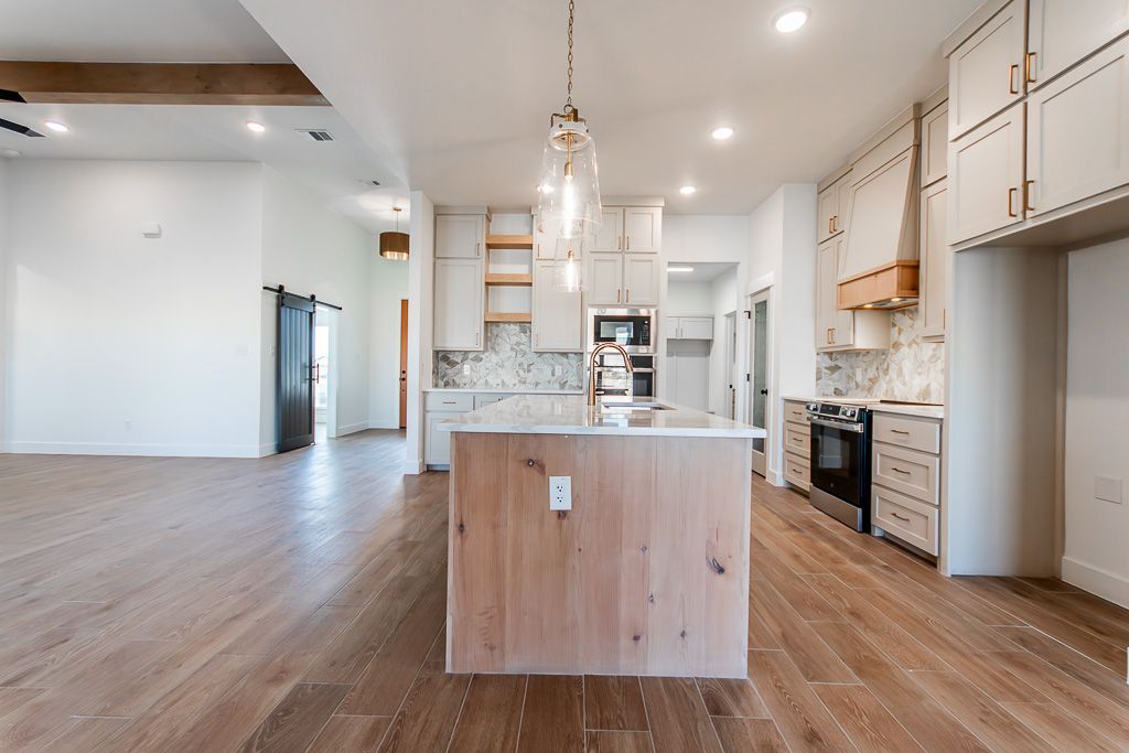 Spacious kitchen with wood floors and island. White cabinets, stainless steel appliances, open shelving, and pendant lights.