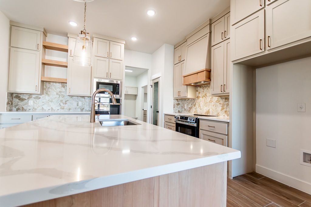 Modern kitchen with light-colored cabinets, marble backsplash, large island, and built-in appliances.