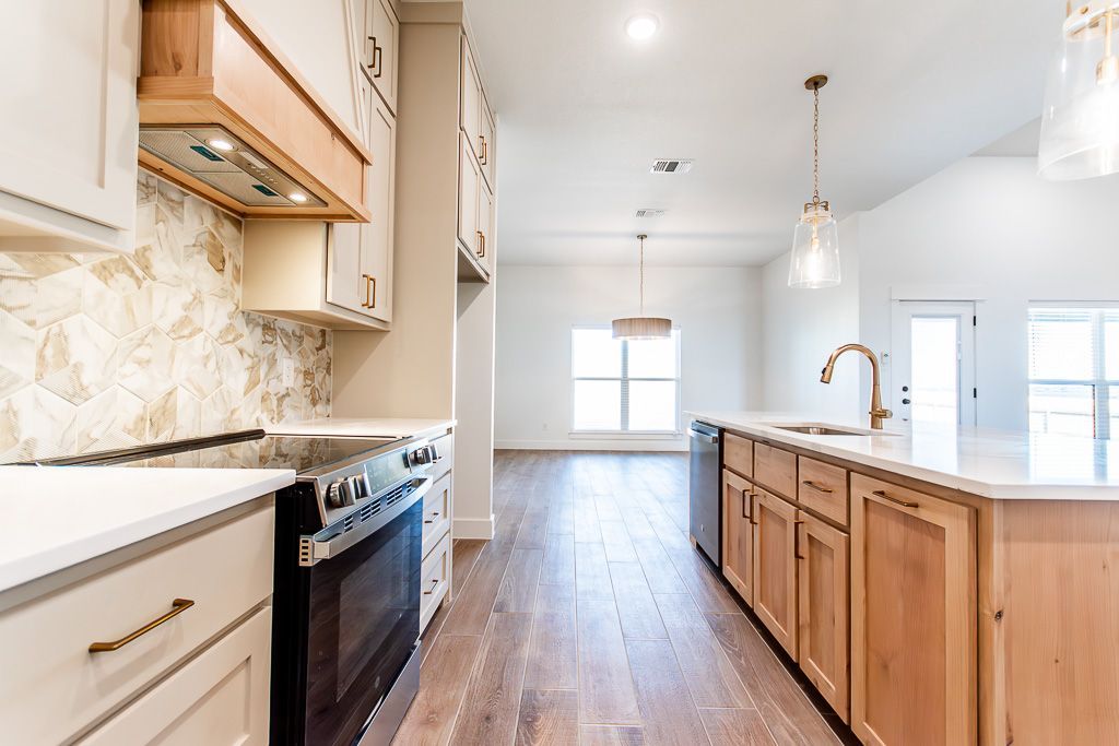 Modern kitchen with light wood cabinets, dark range, and island with a sink.
