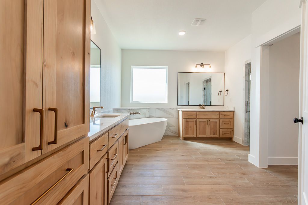 Bathroom with light wood cabinets, white bathtub, and light-colored wood floor.