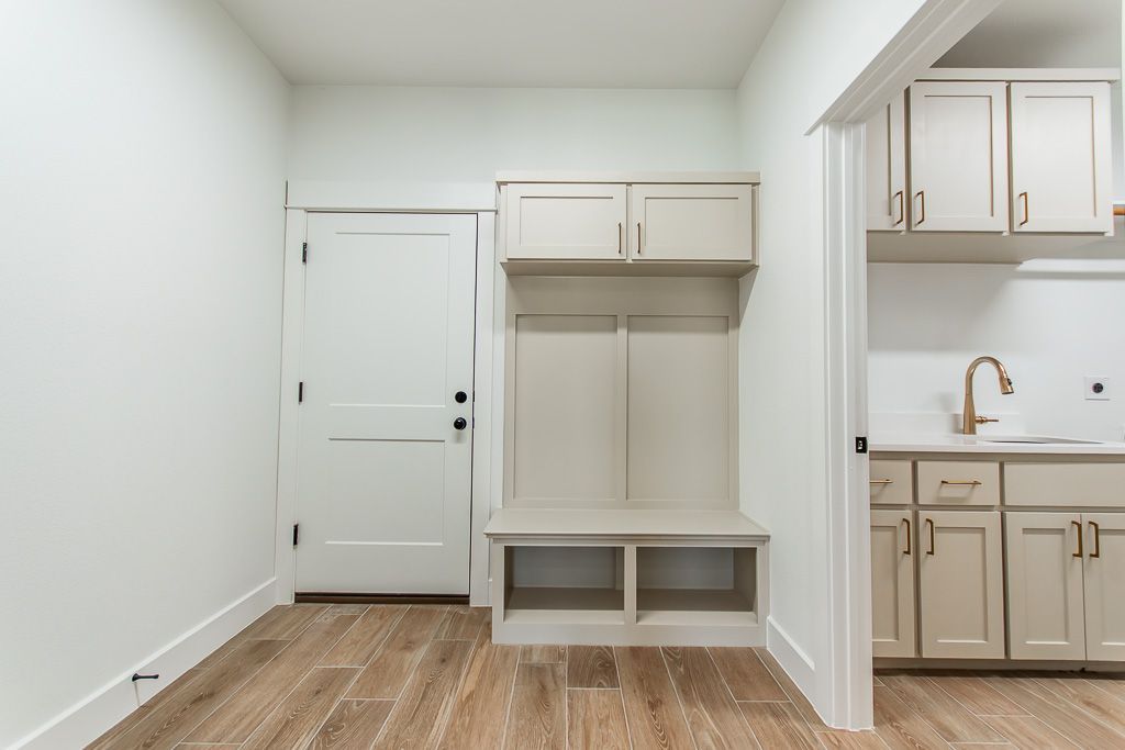 Mudroom with built-in storage bench, cabinets, and a doorway to a laundry room with a sink and cabinets.