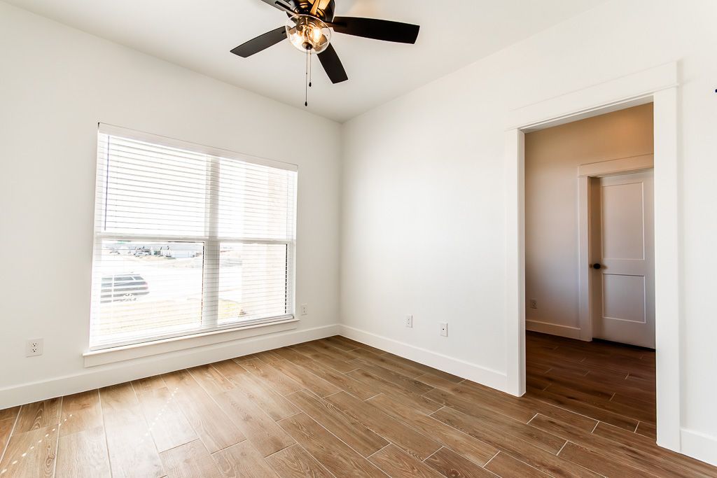 Empty room with wood floors, white walls, large window, and open doorway.