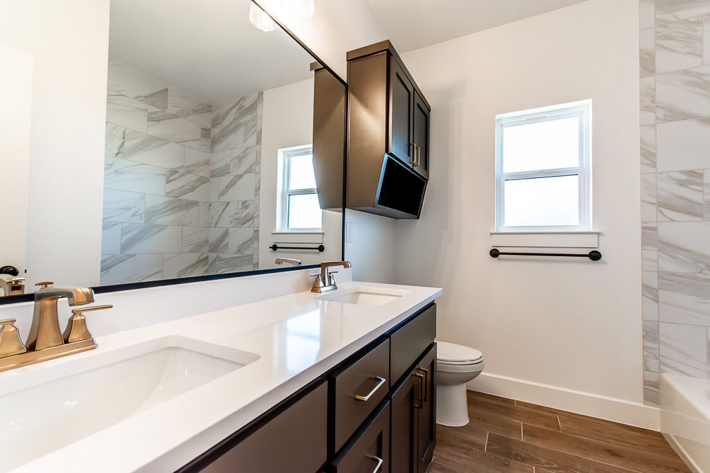Bathroom with a white countertop, dark cabinets, a large mirror, and a window.