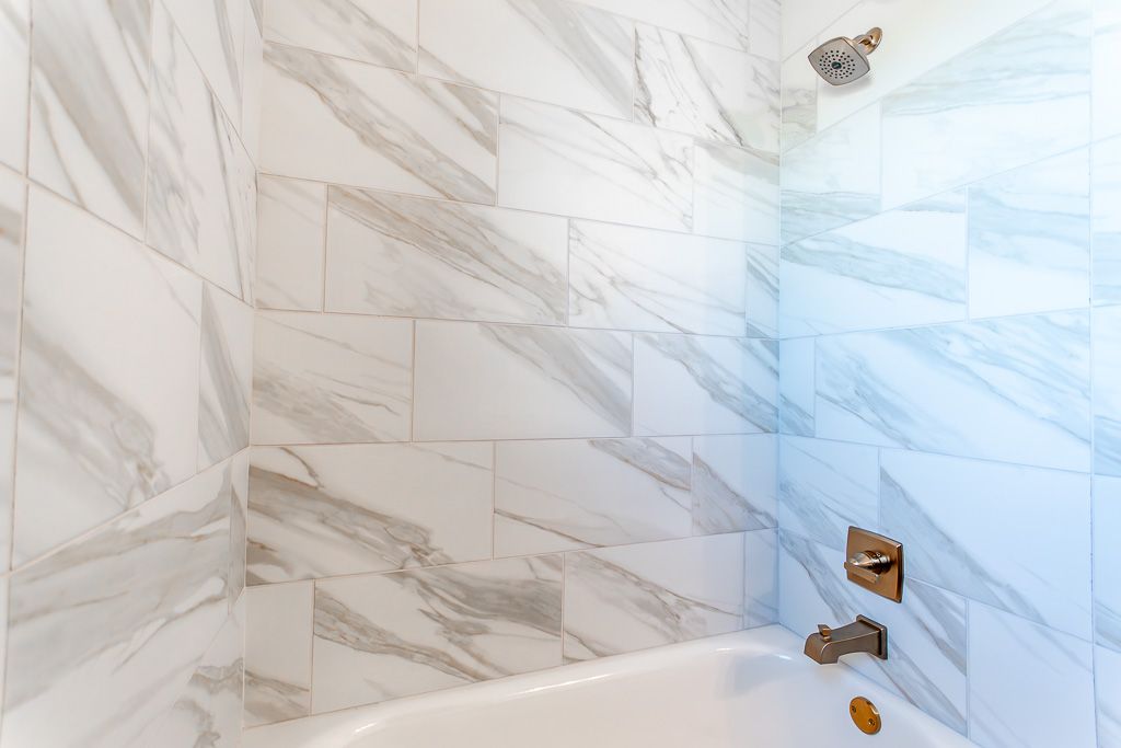 White marble tiled shower with gold fixtures and a white bathtub.