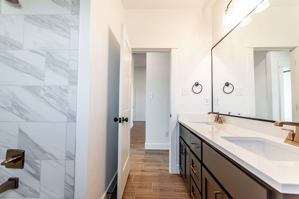 Bathroom with marble-tiled shower, white walls, dark vanity, and a doorway leading to another room.