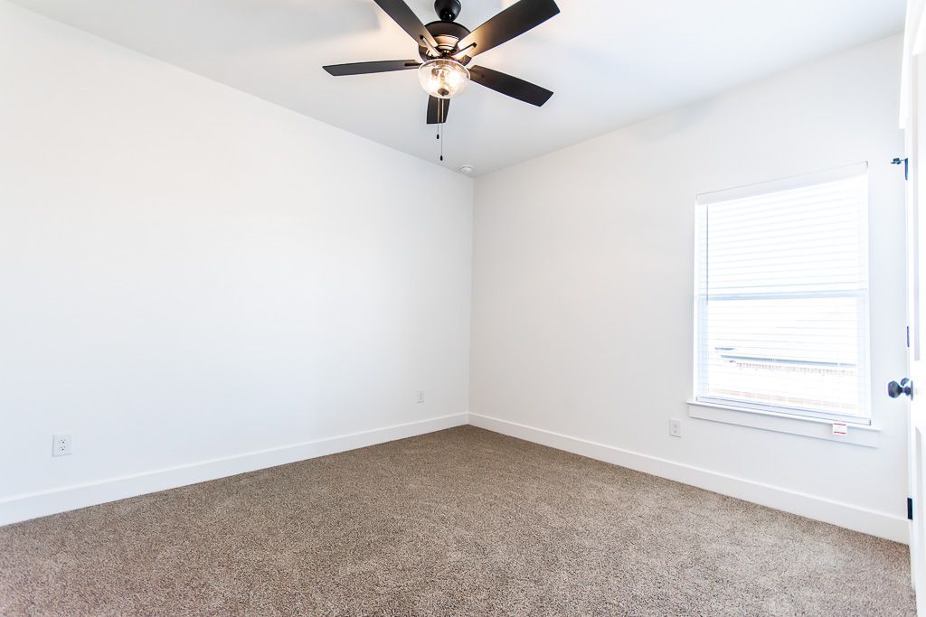 Empty bedroom with beige carpet, white walls, ceiling fan, and window.