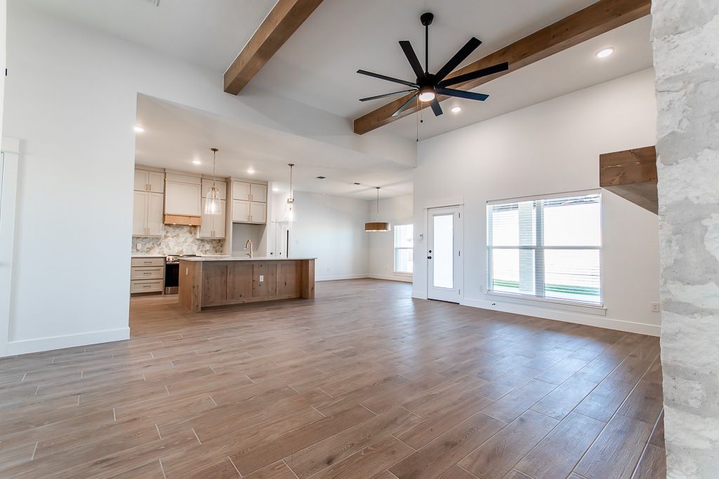 Open-concept living space with wooden floors, kitchen, and exposed beams; high ceilings, natural light.