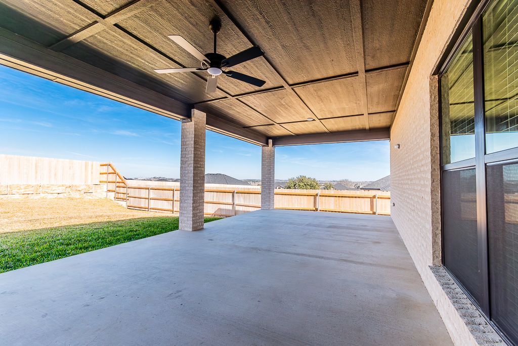 Covered concrete patio with ceiling fan, looking towards a fence and blue sky.