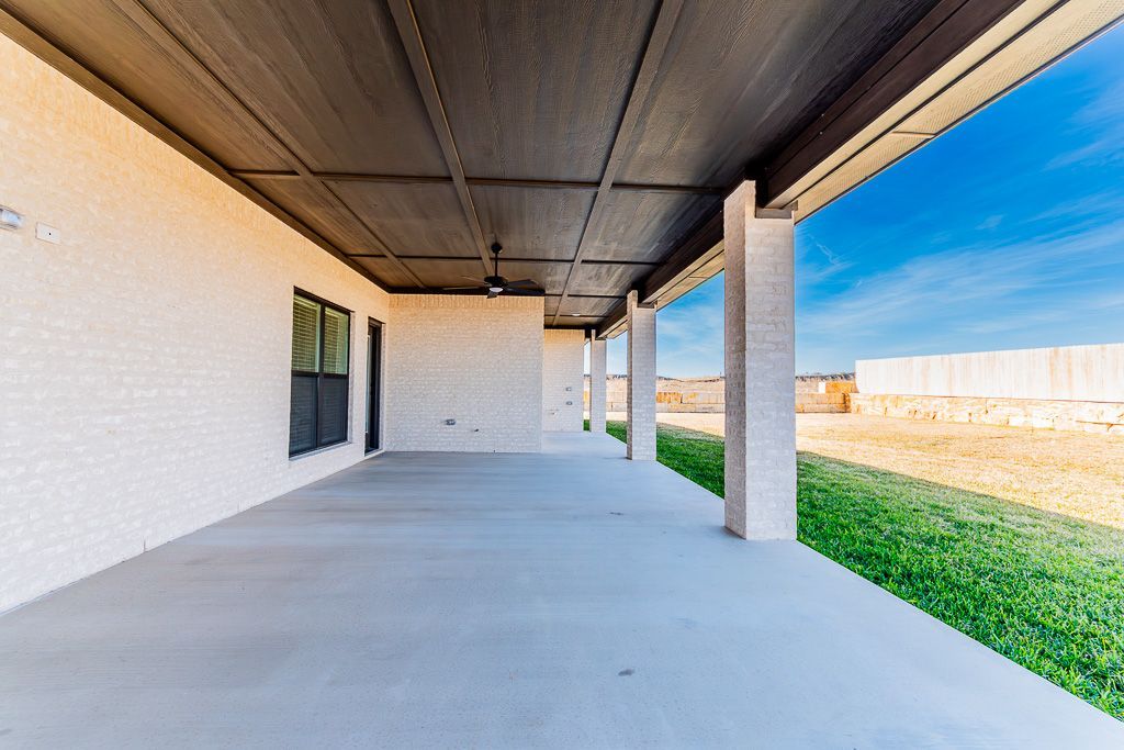 Covered concrete patio with white walls, dark ceiling, and a green lawn.
