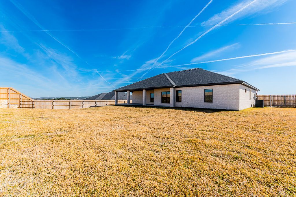A single-story white house with a dark roof and a grassy yard under a blue sky with contrails.