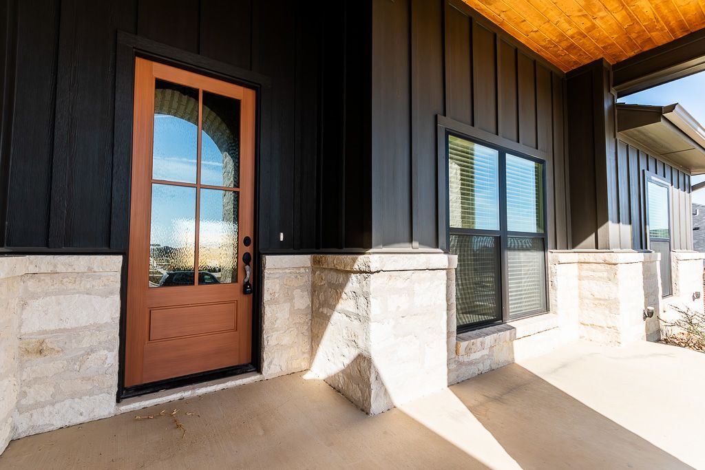 Brown door with arched glass, surrounded by dark siding and light stone columns.