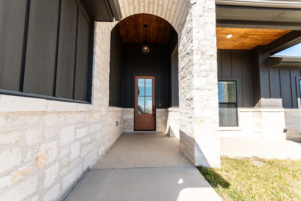 Entryway of a house with stone walls, dark door, and arched ceiling. Concrete walkway and grass visible.