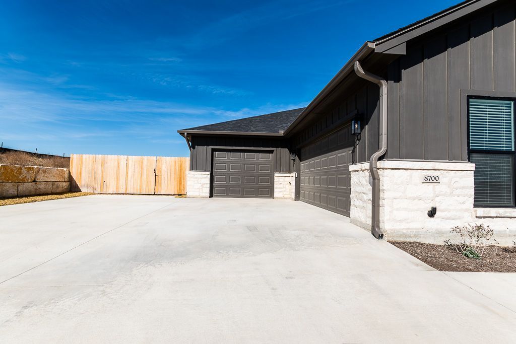 Gray house with black garage door, light stone accents, and wooden fence against a bright blue sky.