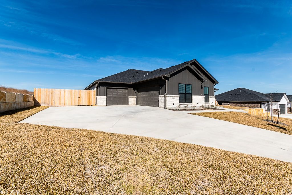 Modern house with black exterior, two-car garage, long driveway, and wood fence against a blue sky.