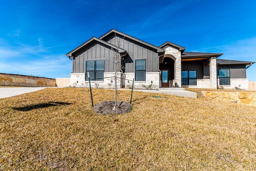 Modern, single-story house with gray siding, two-car garage, and dry, brown grass lawn.