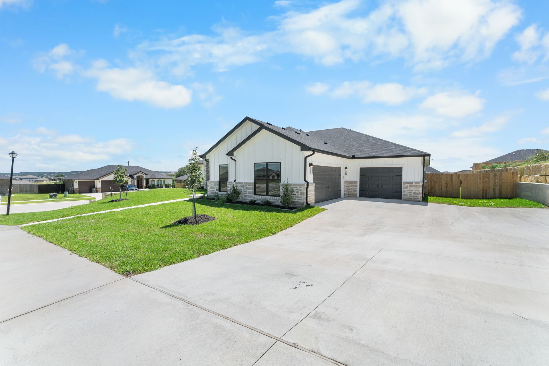 White house with a two-car garage and concrete driveway, blue sky, grassy lawn, and surrounding neighborhood.