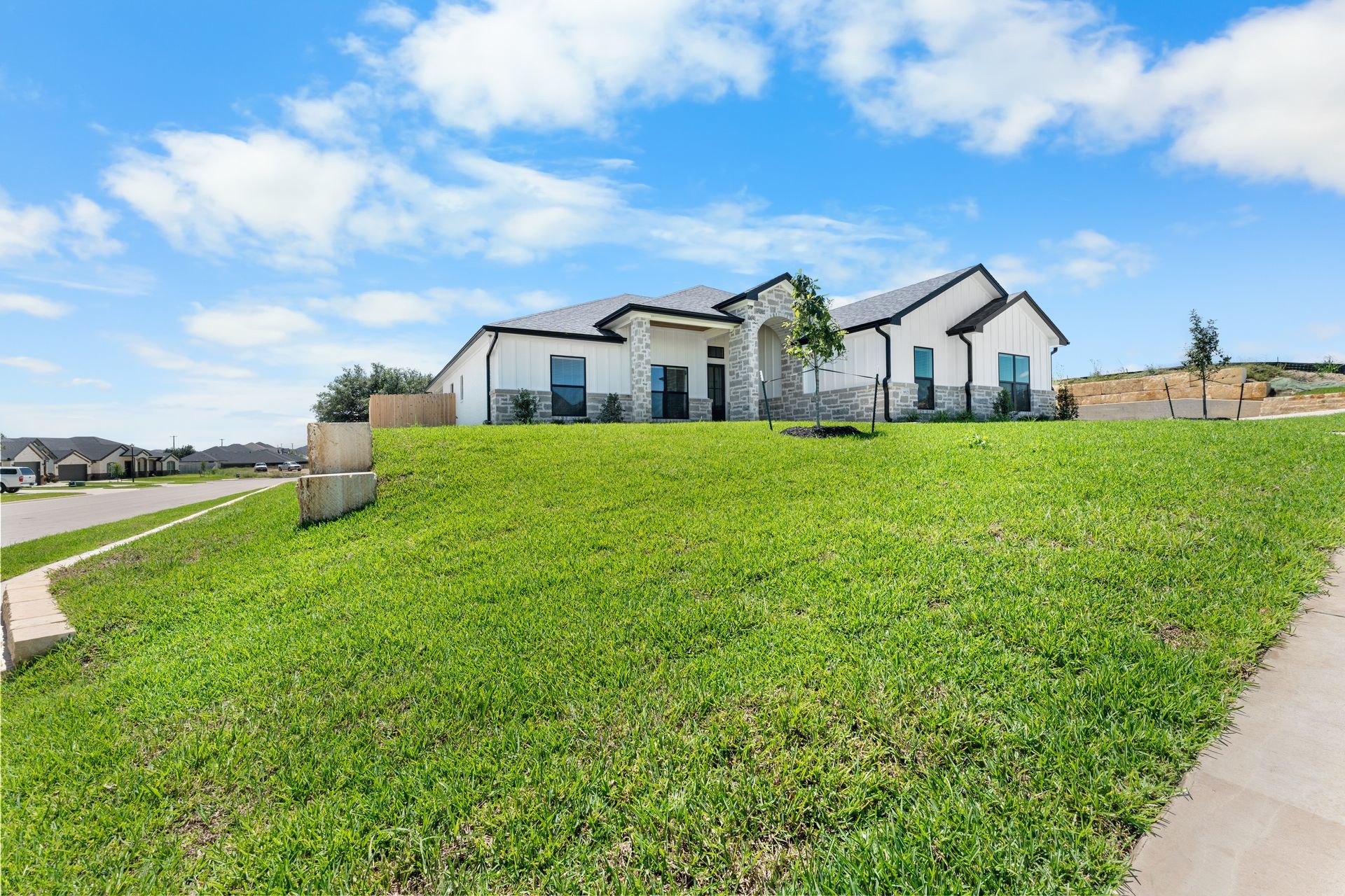 White house on a grassy hill under a blue sky with scattered clouds.