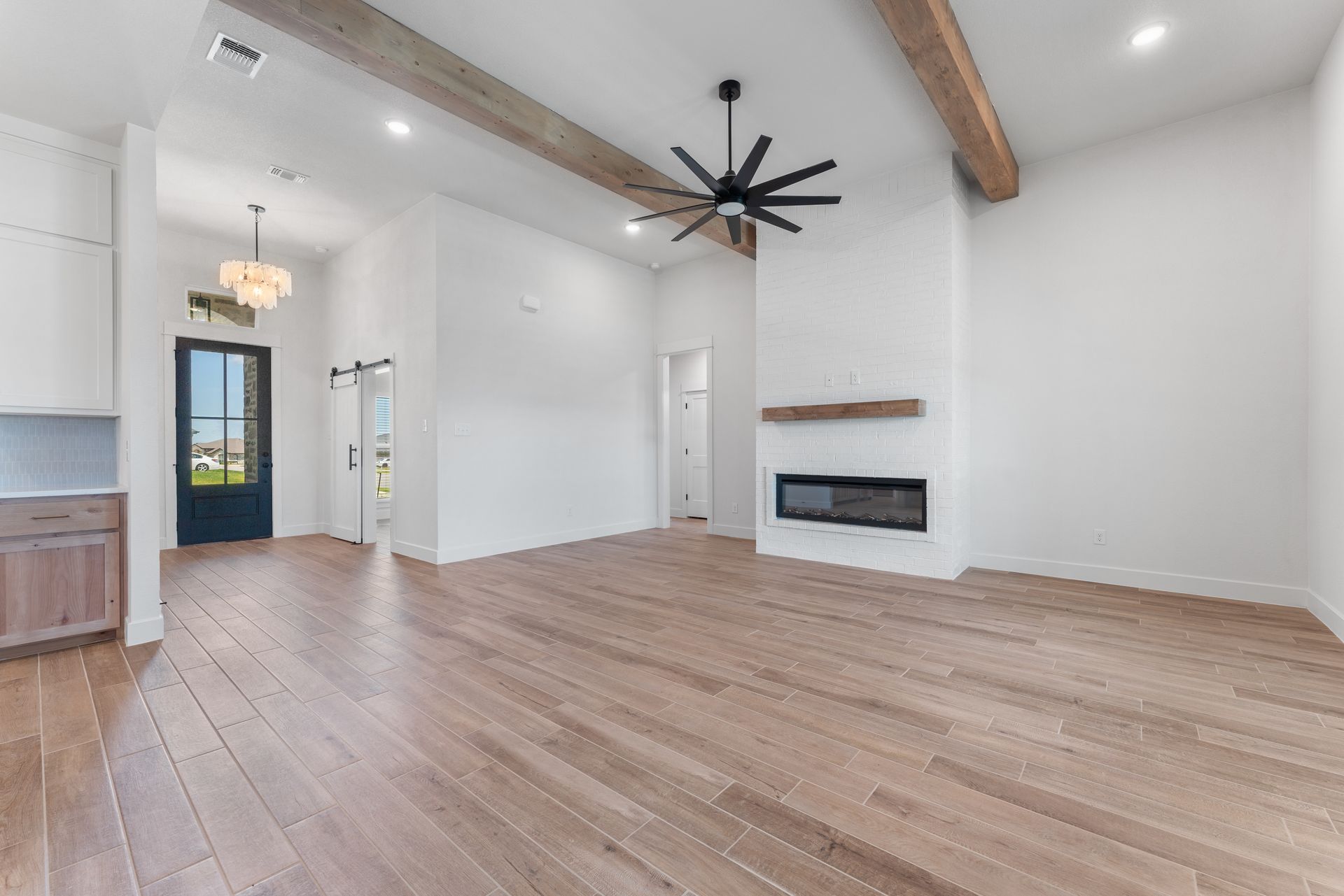 Spacious living area with wood floors, white walls, a fireplace, and exposed wooden beams.