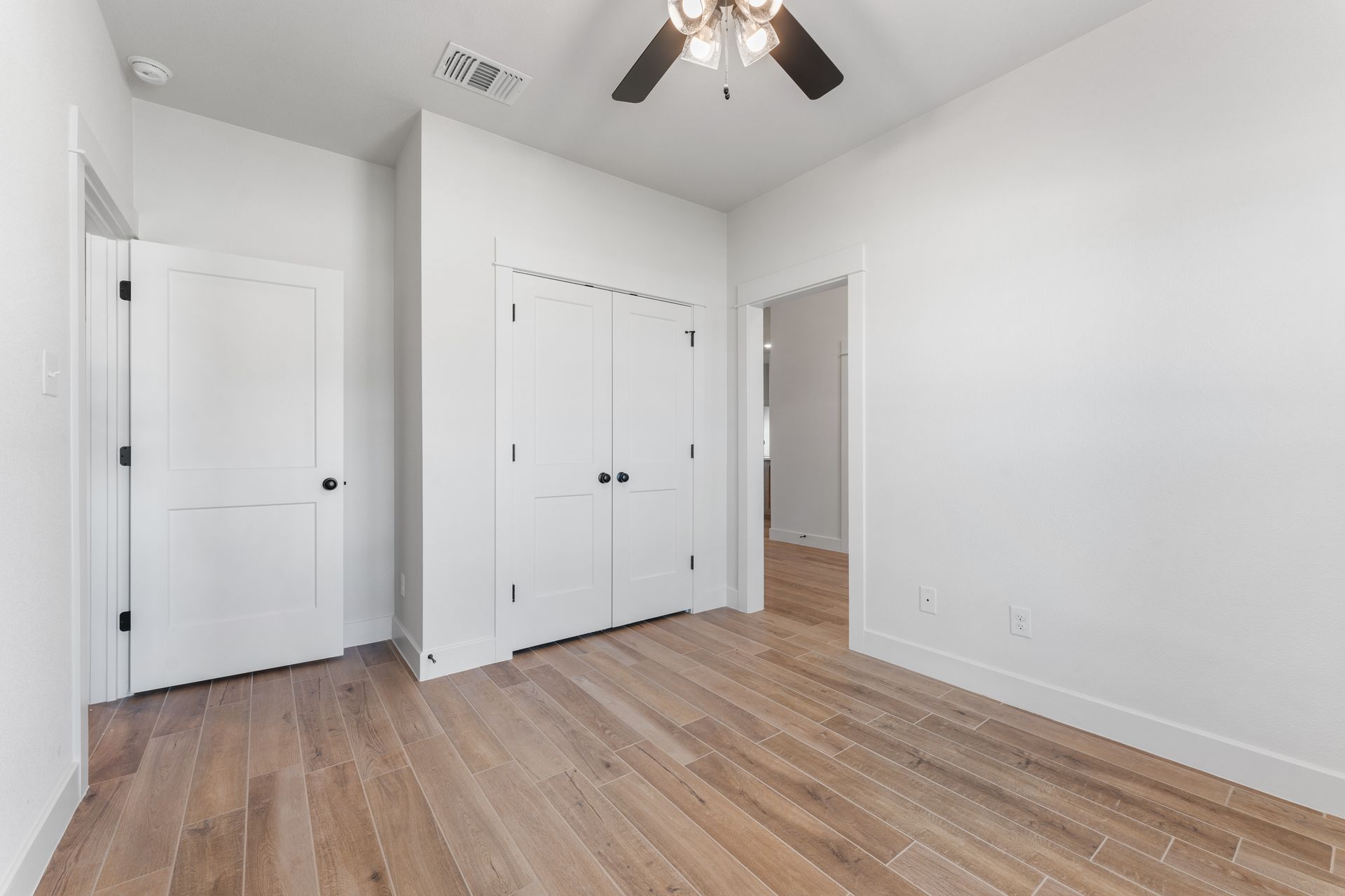 Empty room with wood floors, white walls, two doors, and a closet. Ceiling fan.
