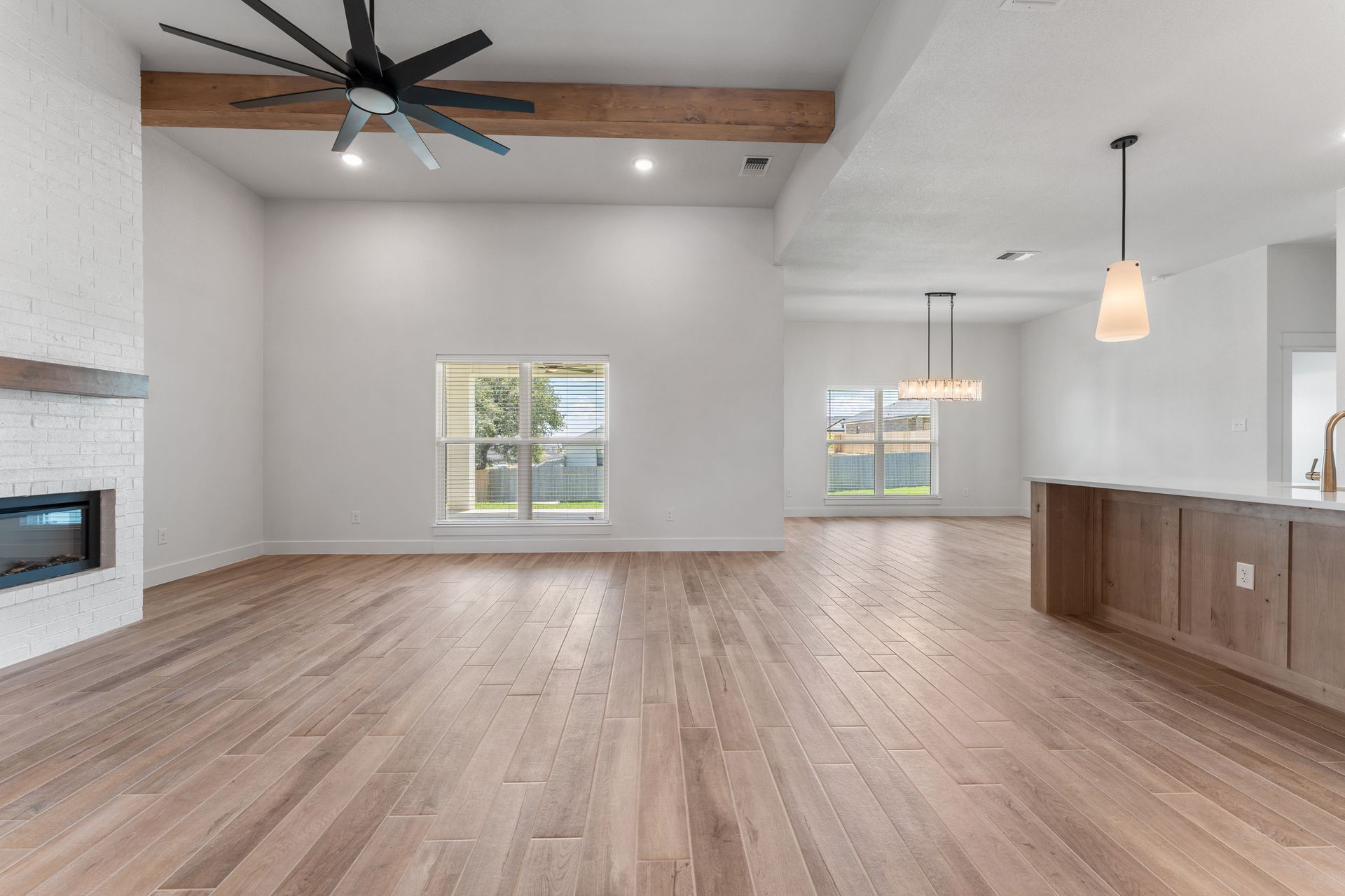 Empty, light-filled living room with hardwood floors, white walls, fireplace, and windows.