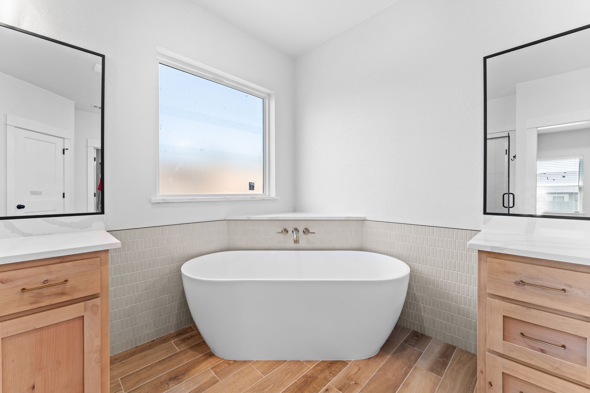 Bathroom with freestanding white tub, wood floor, and two vanities with mirrors.