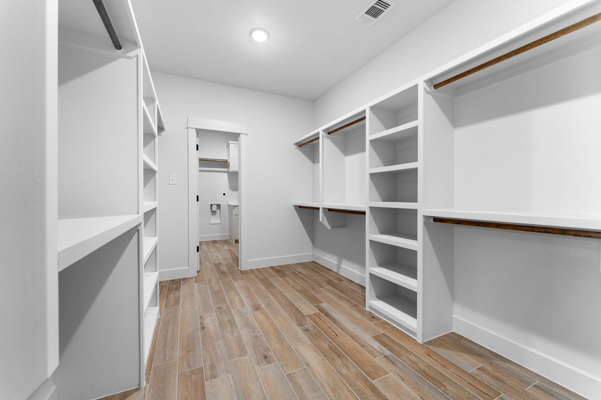 Empty white walk-in closet with shelves and wood flooring.