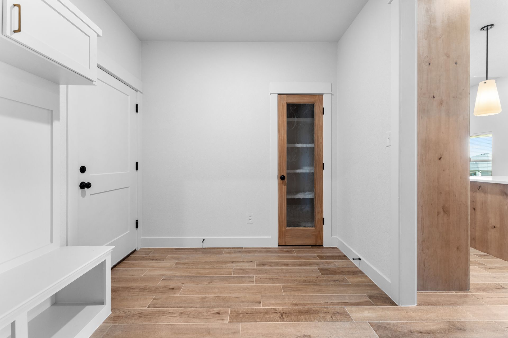 Bright entryway with white walls, wood floors, and a wooden door with glass panels.