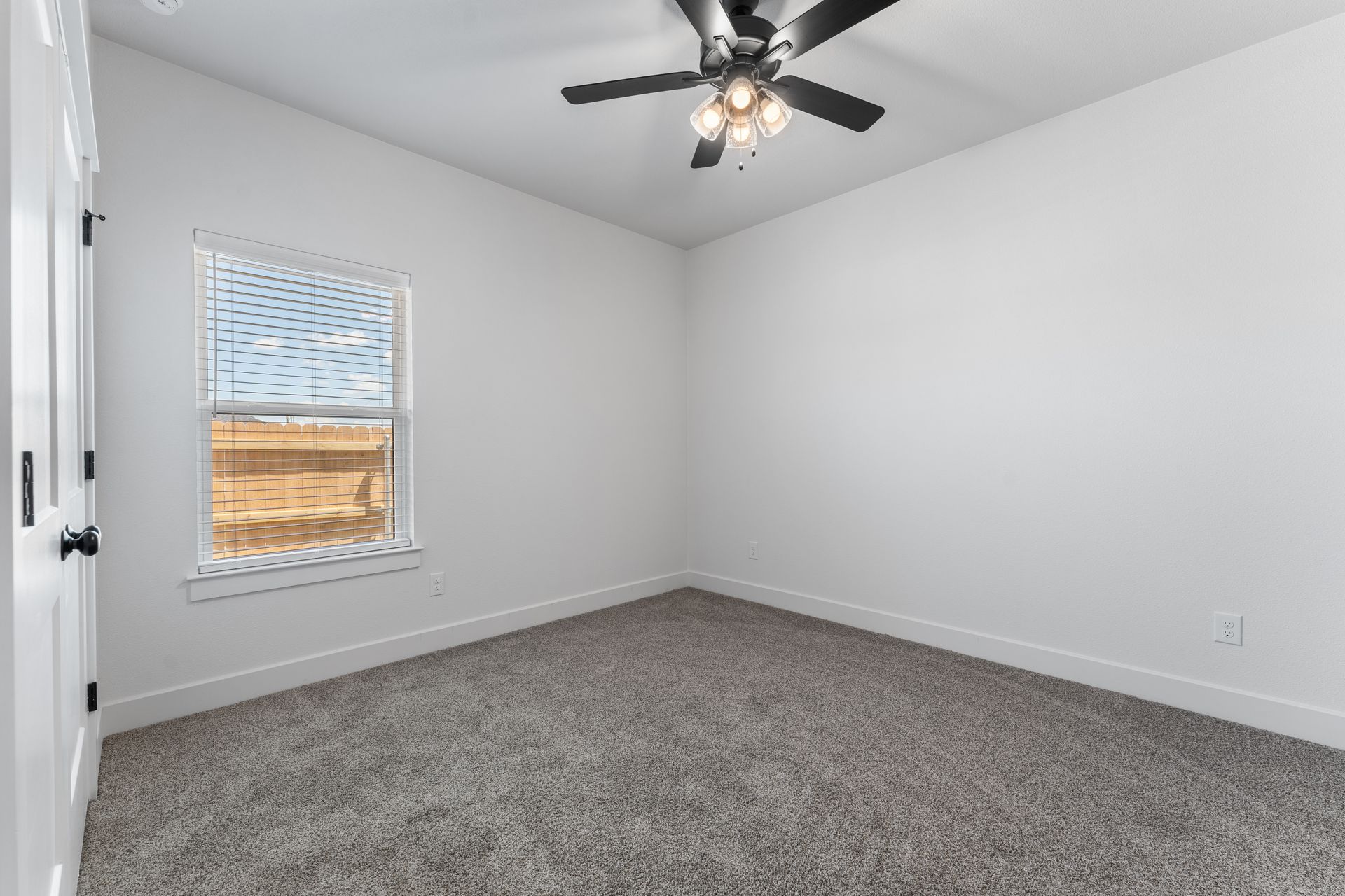 Empty room with gray carpet, white walls, window, and ceiling fan.