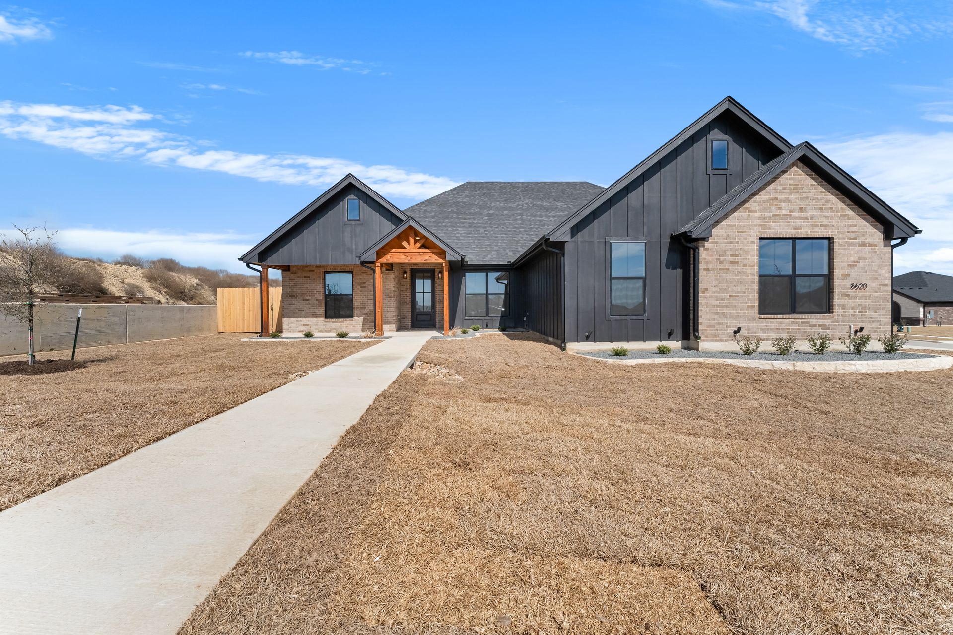 Modern suburban house with a brick and black vertical-siding exterior, a front walkway, and an open, sunny yard.