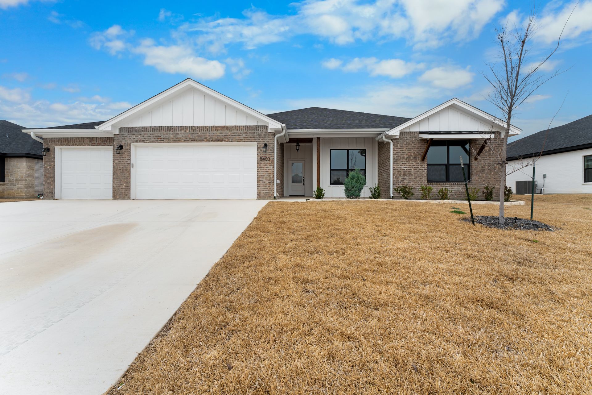 A single-story brick house with a white garage door and a concrete driveway under a blue sky.